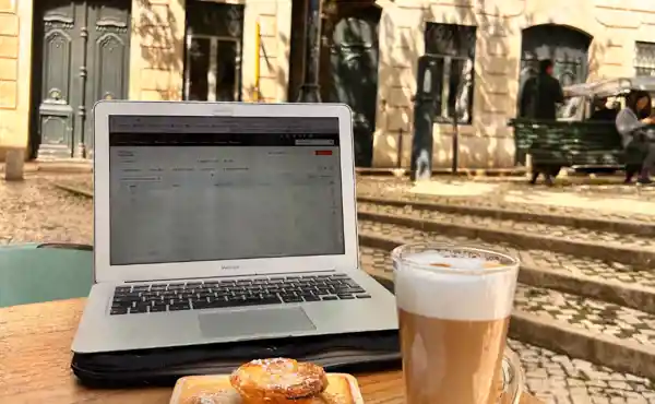 Macbook met latte macchiato en pastel de nata op een terras tafeltje in een stad