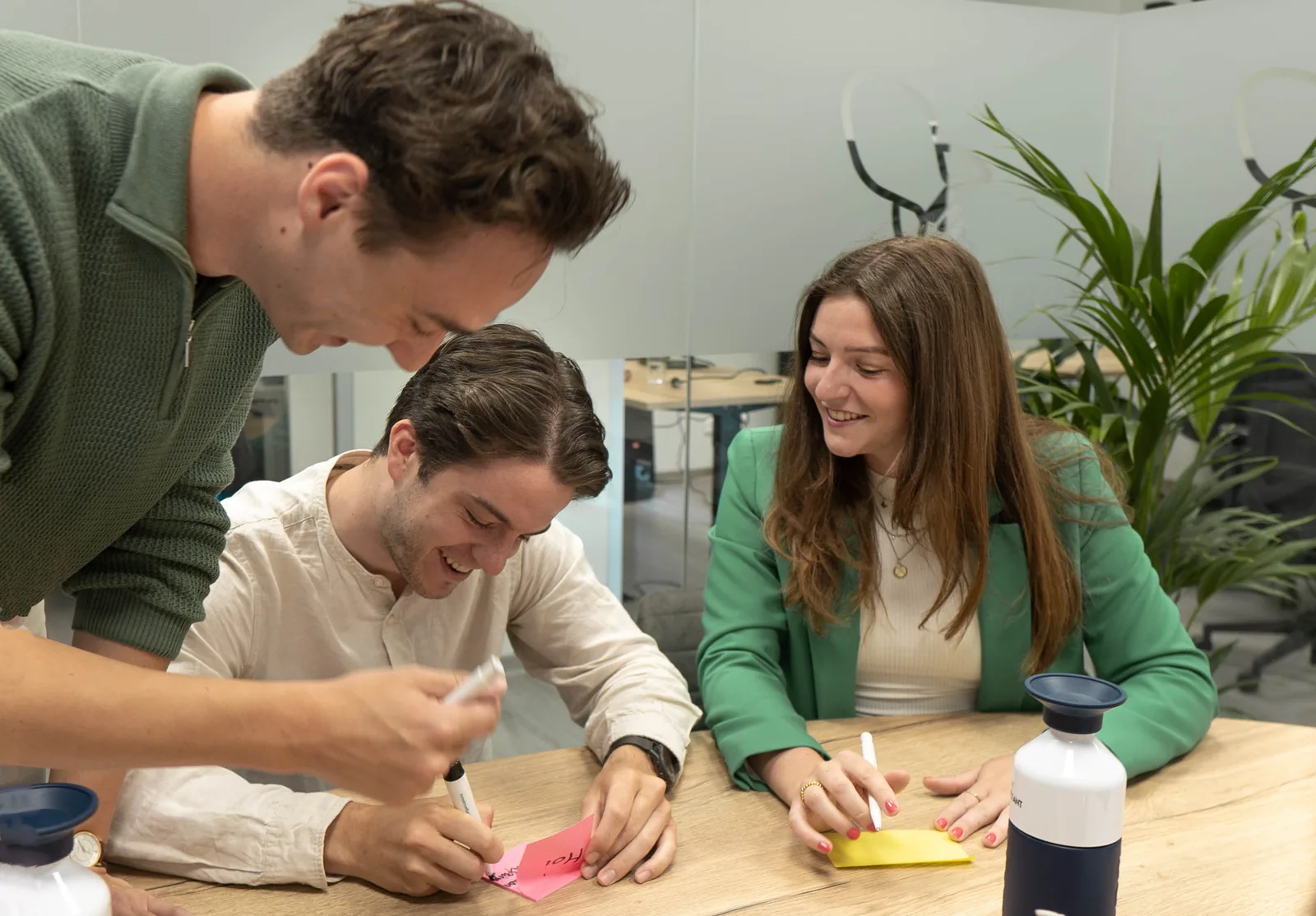 Three student consultants laughing as they work together at a table with sticky notes